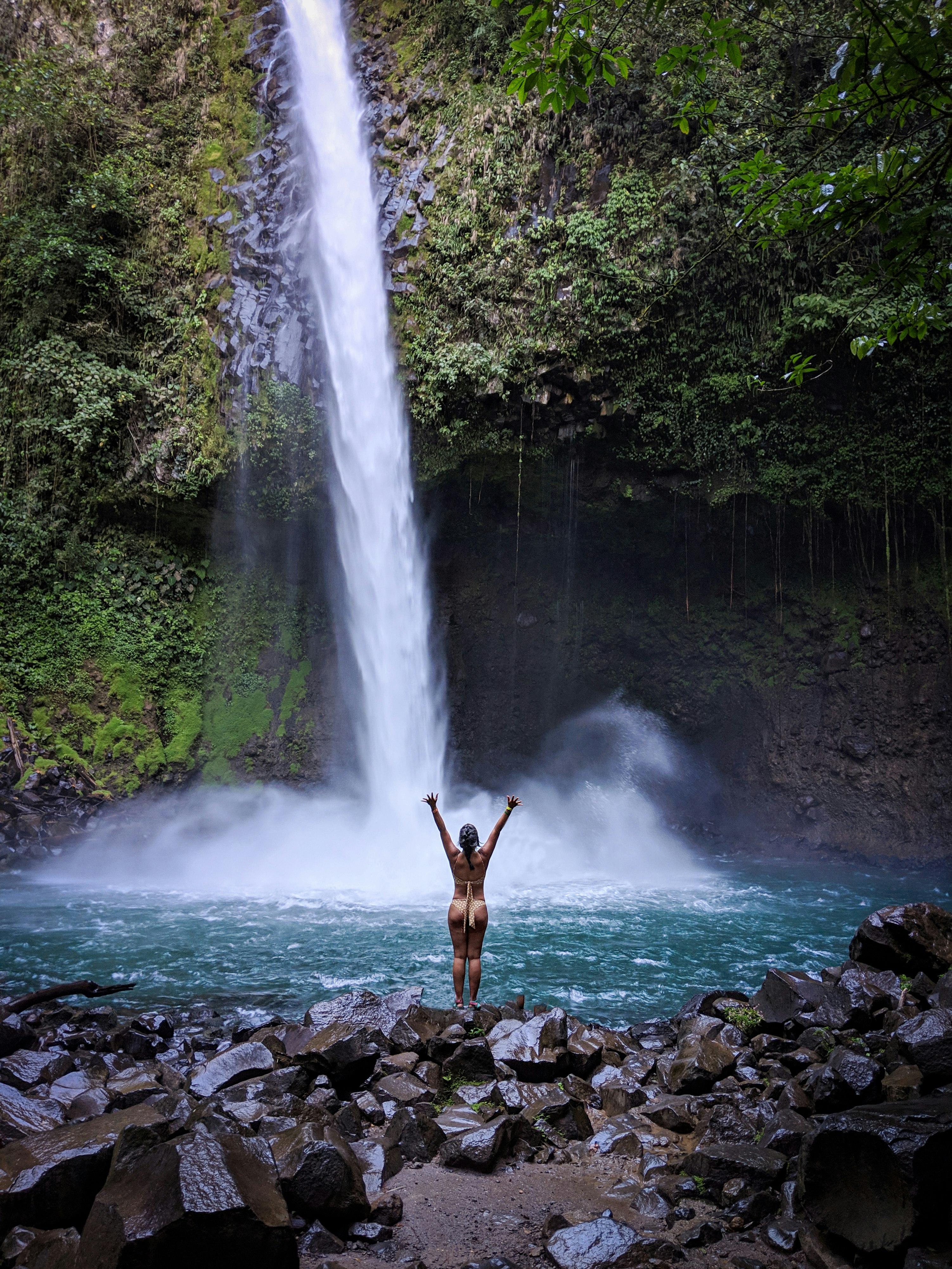 man standing on rocky shore near waterfalls during daytime